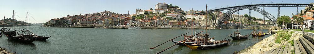 Panorama der Stadt Porto; rechts die Ponte Dom Luís I; links der Bildmitte das historische Altstadtzentrum (Ribeira) mit dem Torre dos Clérigos im Hintergrund; auf der äußersten linken Seite die Arrábida-Brücke; außerdem sind auf dem Bild die oft für den Portwein-Transport benutzten Rabelo-Boote zu sehen. (Juni 2006)
