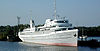 Steuerbordseite eines grau-weißen Schiffes mit zwei Rettungsbooten, vie Decks und einem kleinen Schornstein, das am Pier festgemacht ist