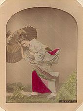 Eine Studioaufnahme, die von Kimbei gemacht wurde und eine Japanerin mit Schirm zeigt, die sich damit vermeintlich gegen den Wind schützt. Ihr Unterrock wird mithilfe von Drähten freigelegt, sodass der Eindruck, es sei windig, verstärkt wird.