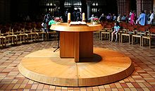 Foto des hölzernen Altars, der mittem im Raum auf einem flachen runden Holzpodest steht