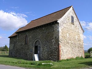 Eine schlichte steinerne Kirche mit Ziegledach von Nordosten gesehen; das Kirchenschiff mit dem runden Torbogen und dahinter der kleinere Altarraum