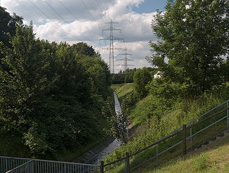 Der Schmiedesbach zwischen dem Düker unter dem Rhein-Herne-Kanal und der Mündung in die Emscher. Im Hintergrund die Brücke der Zechenbahn zum Westhafen Wanne und die Rohrleitungen der Fernwärmeschiene Ruhr